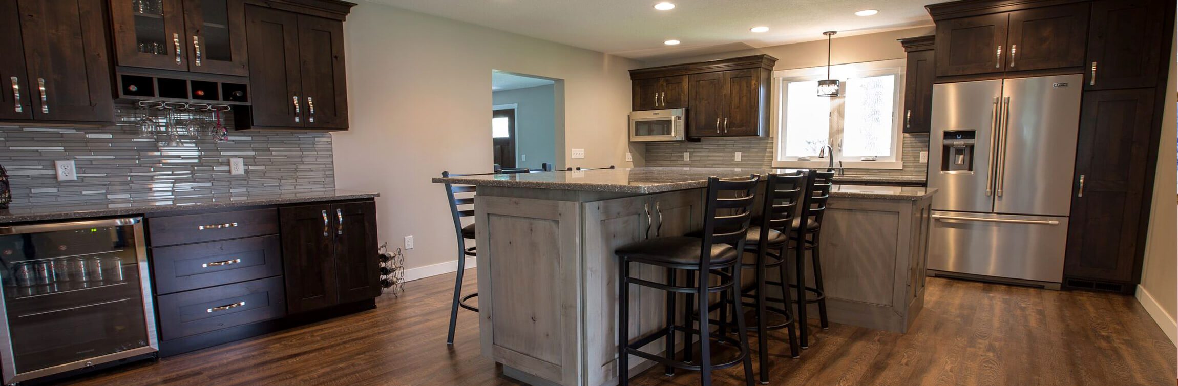 Custom Residential Kitchen & Bar Station featuring dark-stained solid wood cabinets, glass tile backsplash, large center island, stone countertops, and hardwood flooring